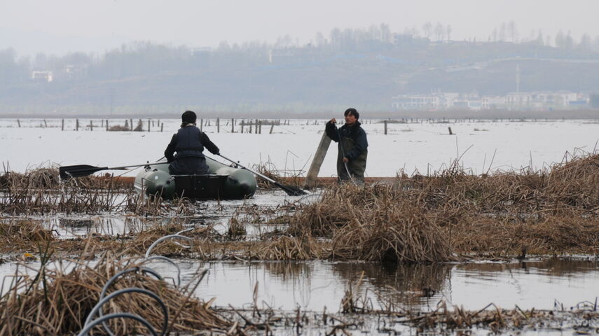 Zwei Arbeiter im Wetland mit einem Schlauchboot sind dabei, die Drausy® Belüftungslinien zu kontrollieren. Im Hintergrund sieht man den Caohai-See