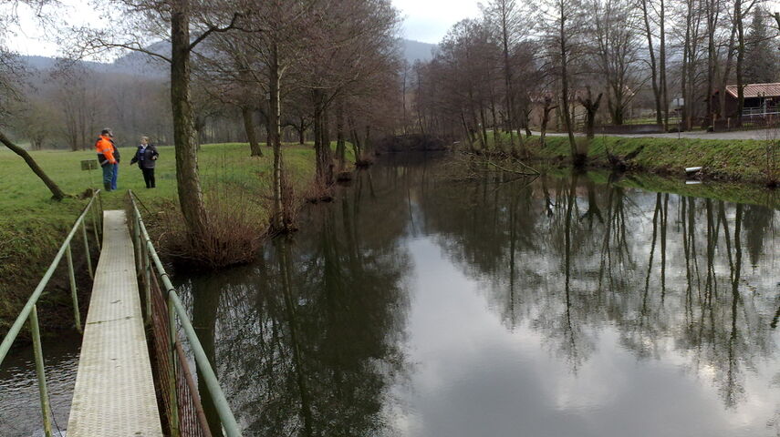 Vue sur le Tankgraben Malsch: un pont se trouve au coude du fossé, on voit des arbres riverains en ligne et un petit groupe de personnes en arrière-plan